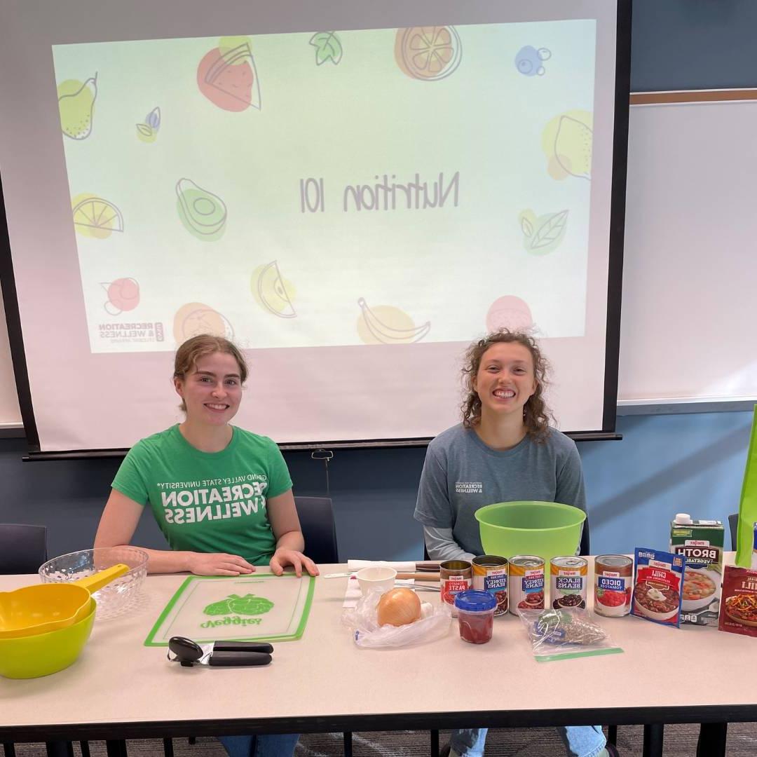 Two WIT peer educators in front of Nutrition 101 presentation doing a food demo